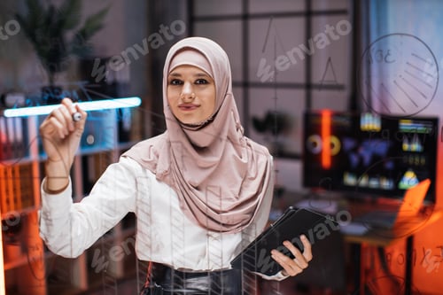 Preview: Close up through the glass view of focused young muslim businesswoman drawing pie chart