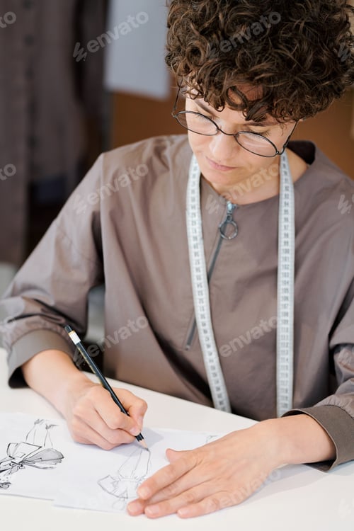 Preview: Young serious female sketching new fashion models on paper