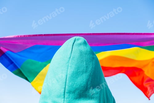 Preview: Person in a green hoodie with a rainbow flag in the background on a clear sunny day