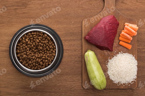 Preview: top view of dry pet food in silver bowl near raw meat, zucchini, rice and carrot on wooden table