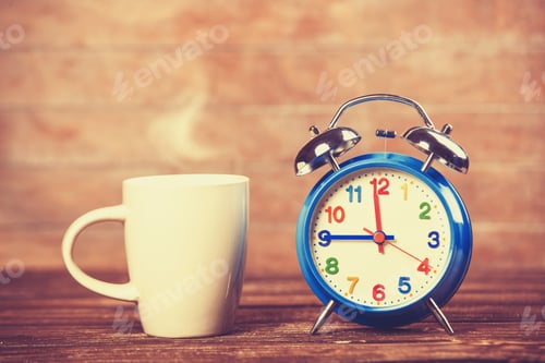 Preview: Cup of coffee and alarm clock on wooden table.
