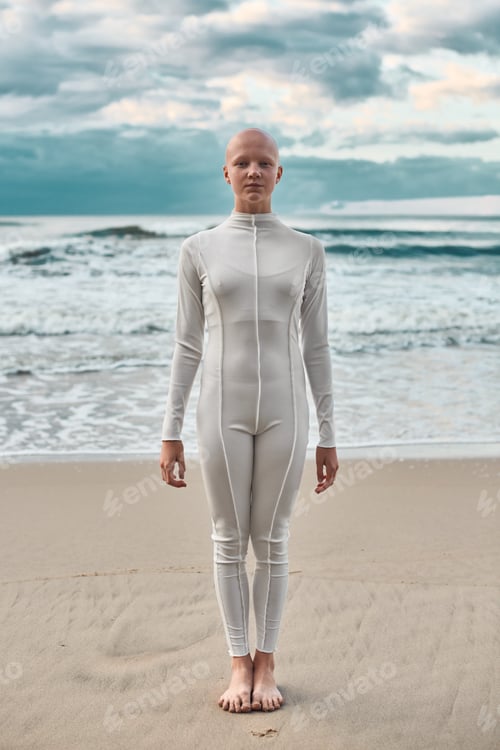 Preview: Full length portrait of young hairless girl with alopecia in futuristic suit standing on seashore