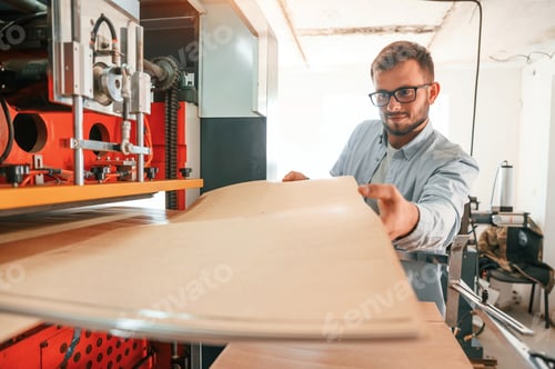 Preview: Working with wooden sheets. Man in print house that in white clothes is indoors
