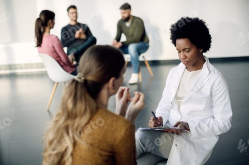 Preview: African American psychotherapist taking notes while talking to female patient.
