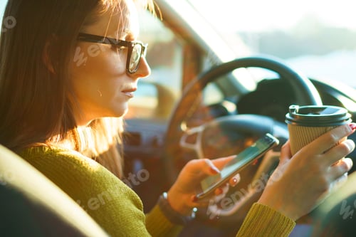Preview: Woman using smartphone and drinking coffee while sitting in a ca