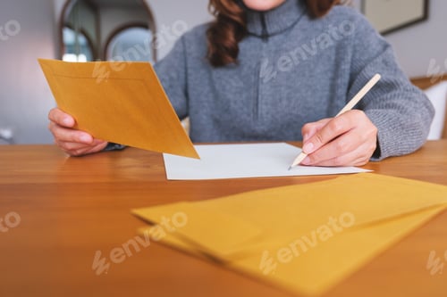 Preview: Closeup image of a young woman writing on a letter and envelopes