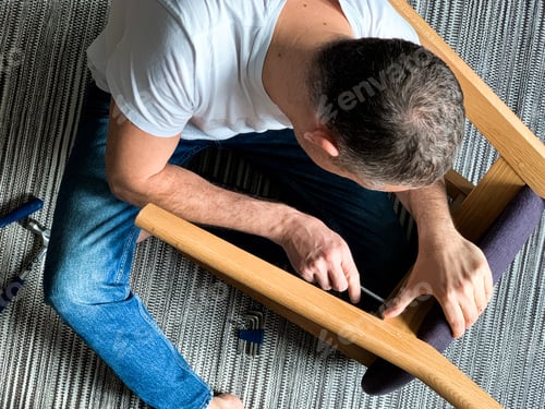 Preview: Middle aged man is fixing wooden chair at home with using screwdriver. DIY project, home improvement