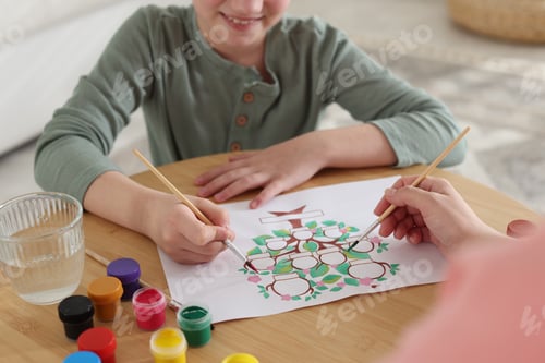 Preview: Girl and her mother drawing family tree with paints at wooden table indoors, closeup