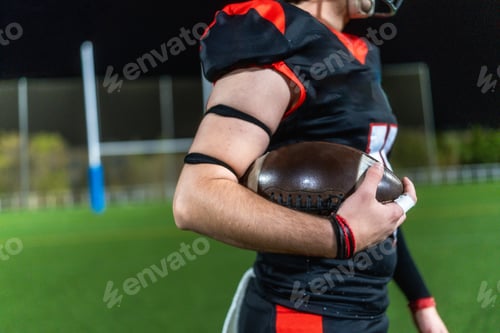 Preview: American football player holding ball on field at night