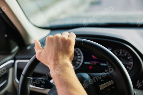 Preview: Hand gripping a steering wheel in a car interior Dashboard instruments are visible in the background