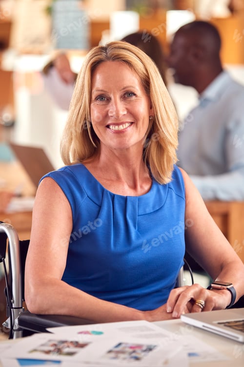 Preview: Portrait Of Mature Businesswoman In Wheelchair Sitting At Desk Working On Laptop In Busy Office