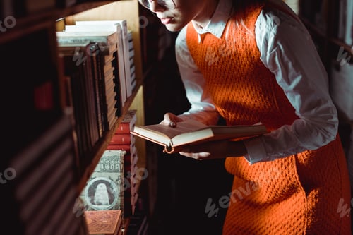 Preview: cropped view of woman in orange dress holding book in library
