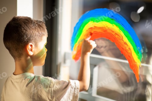 Preview: Caucasian little child draws rainbow with paint on window in elementary school, kindergarten room