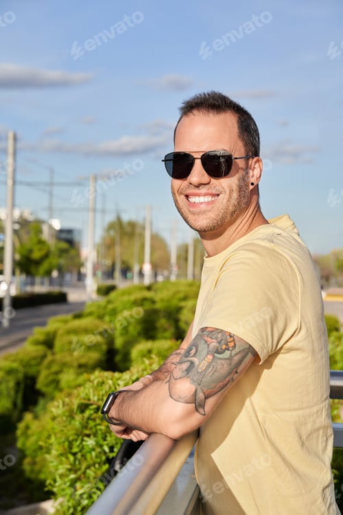 Preview: Man in sunglasses looking at camera and smiling while standing outdoors on a sunny day.