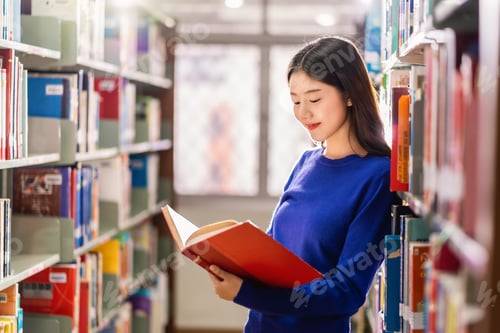 Preview: Asian young Student in casual suit standing and reading the book at book shelf in library
