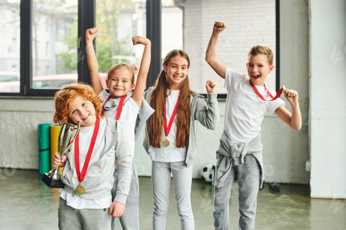 Preview: cheering boys and girls in sportswear posing happily with trophy and golden medals, child sport