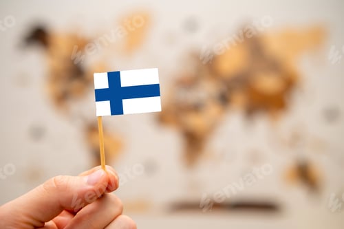 Preview: Finland flag in mans hand on the world map background.