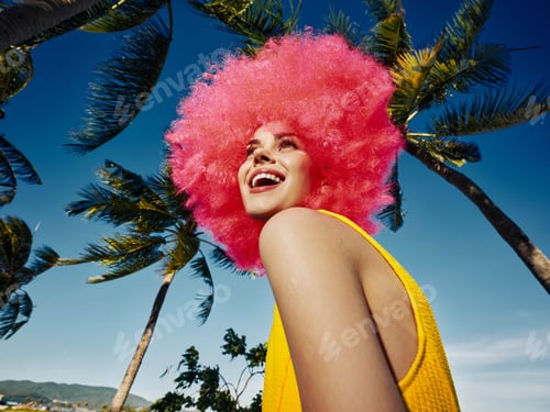 Preview: Pink afro woman standing in front of palm trees, her hair blowing in the wind