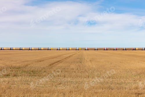Preview: View across a stubble field and the long line of yellow boxcar wagons of a freight train