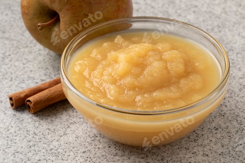 Preview: Glass bowl with organic apple sauce close up with cinnamon and fresh apple on the background