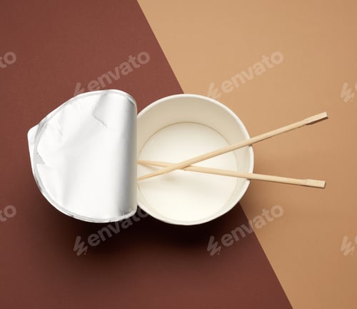 Preview: Open empty noodle bowl with foil lid and pair of wooden sticks on brown background