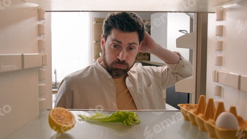 Preview: Hungry man guy open empty refrigerator with half lemon lettuce leaf one egg slice of bread leftover
