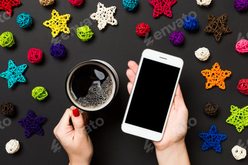 Preview: Top view of a woman holding a phone in one hand and a cup of coffee in another hand