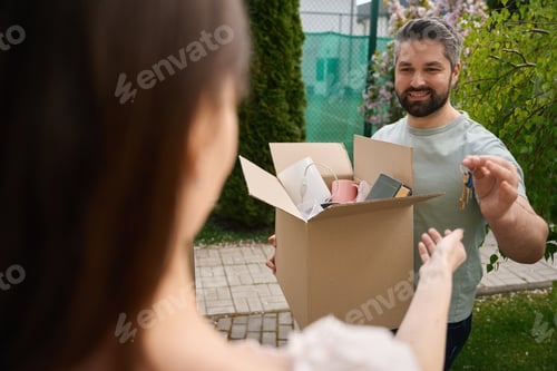 Preview: Young smiling man holding heavy box outside