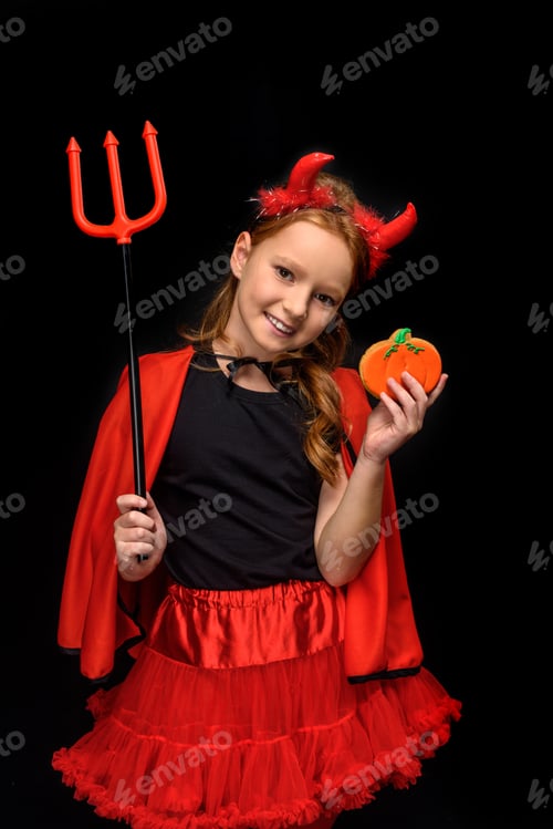 Preview: child in halloween costume of devil with pitchfork and cookie, isolated on black