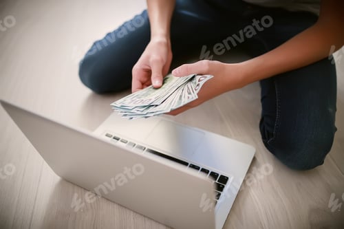 Preview: Hands with a bundle of money. Teenager counts banknotes while sitting by laptop
