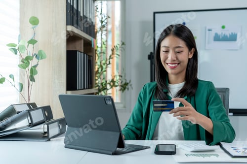 Preview: A woman is sitting at a desk with a laptop and a credit card in her hand
