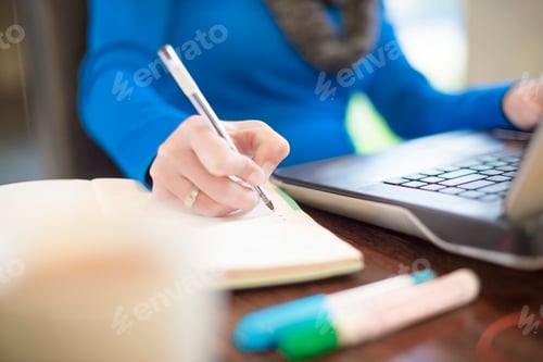 Preview: Woman at desk with laptop writing in notebook