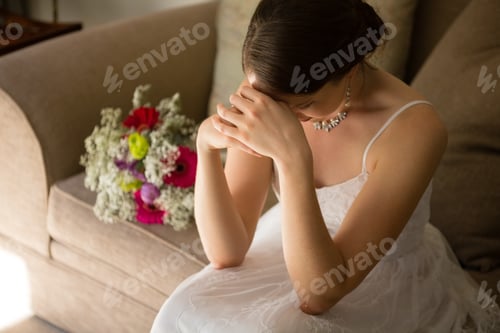 Preview: High angle view of upset bride sitting by bouquet on sofa