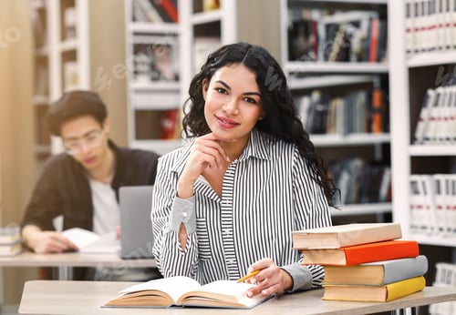 Preview: Cheerful latin girl sitting at desk in library