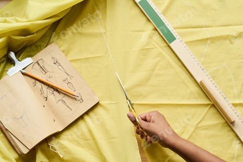 Preview: High angle of hand of tailor holding scissors while cutting textile on table