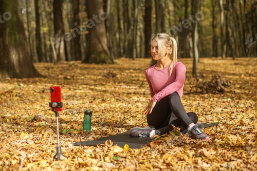 Preview: Woman filming outdoor fitness tutorial in autumn forest.