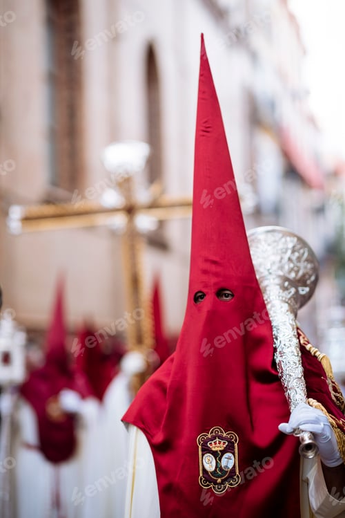 Preview: Hooded figure in traditional procession attire walking through the streets