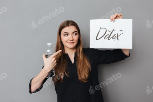 Preview: Smiling lady standing and holding postcard and bottle of water while dreamily looking aside