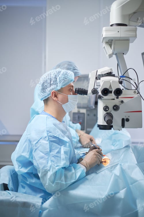 Preview: Middle Aged Male Surgeon Performing Operation Using Surgical Microscope