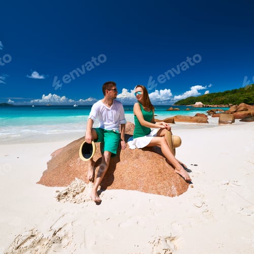 Preview: Couple In Green Sitting On A Rock At Tropical Seychelles Beach