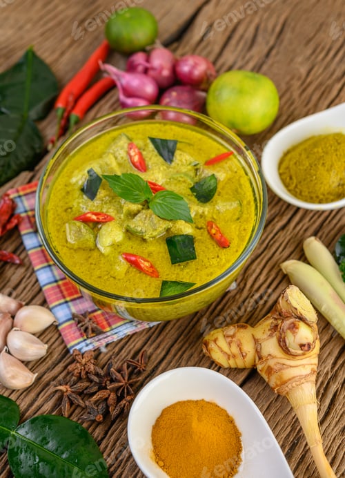 Preview: Green curry in a bowl and spices on wooden table.
