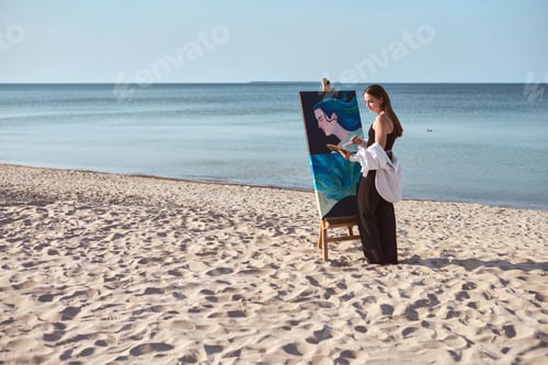 Preview: Young female painter creating art on serene beach