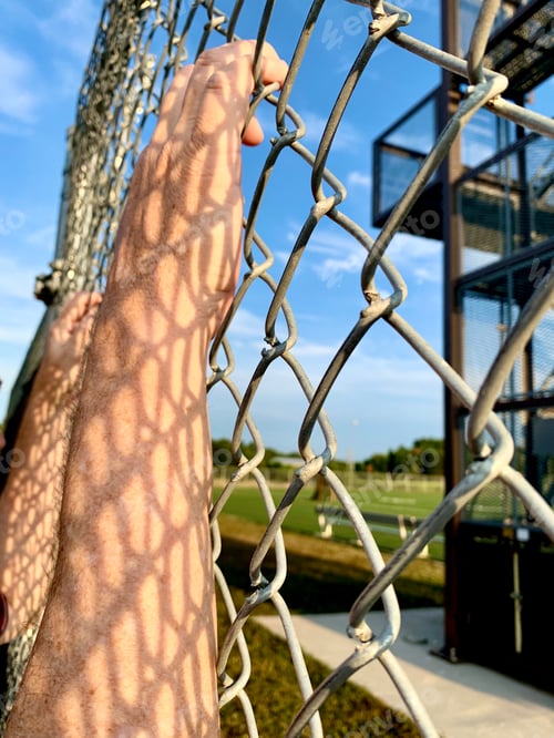 Preview: Person with hands grabbing a wire fence & shadows reflected on arms & hands for trapped concept