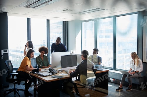 Preview: Creative business team working together in a busy casual office, seen through glass door