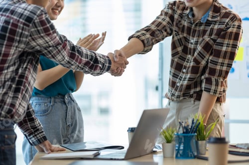 Preview: Young men in casual clothes shaking hands while working in a creative office. Welcome to our team.