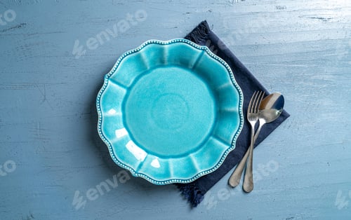 Preview: Top view of a plate with a fork and a spoon on a blue wooden table