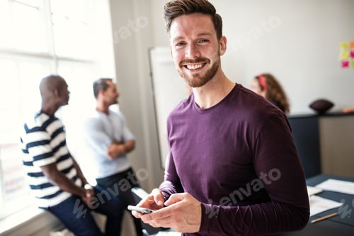 Preview: Smiling young designer using his cellphone after an office meeting