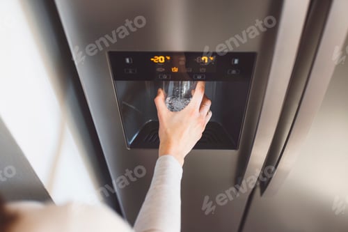 Preview: Caucasian woman pouring her self a glass of cold sparkling water from refrigerators water machine.