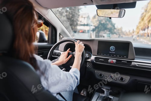 Preview: Woman driving a car with hands on the steering wheel, focused on the dashboard screen displaying
