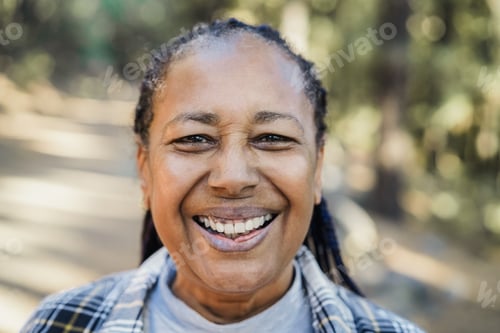 Preview: Senior african woman smiling on camera with forest in background - Focus on face